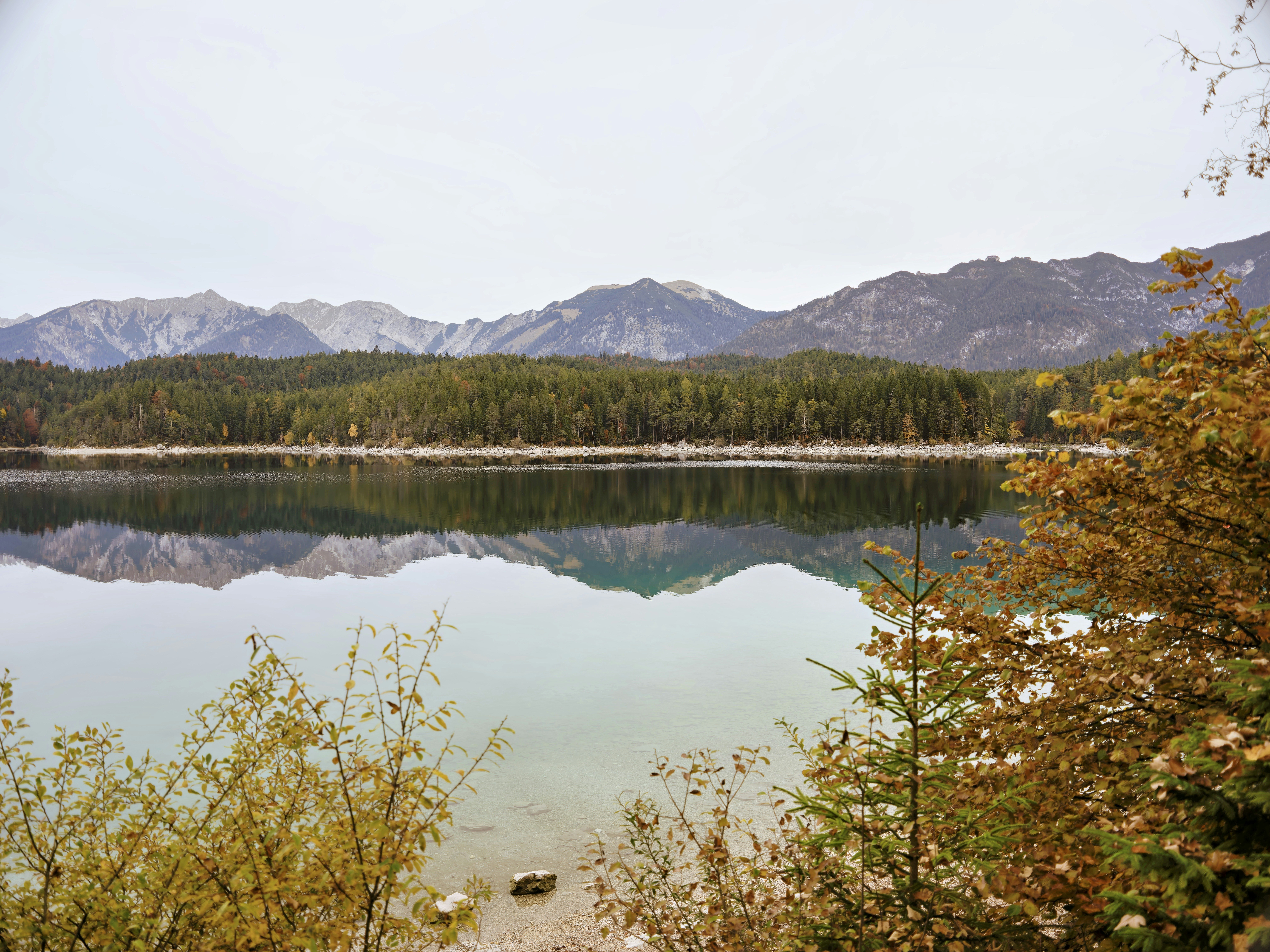 Calm lake reflecting mountains and trees under a cloudy sky