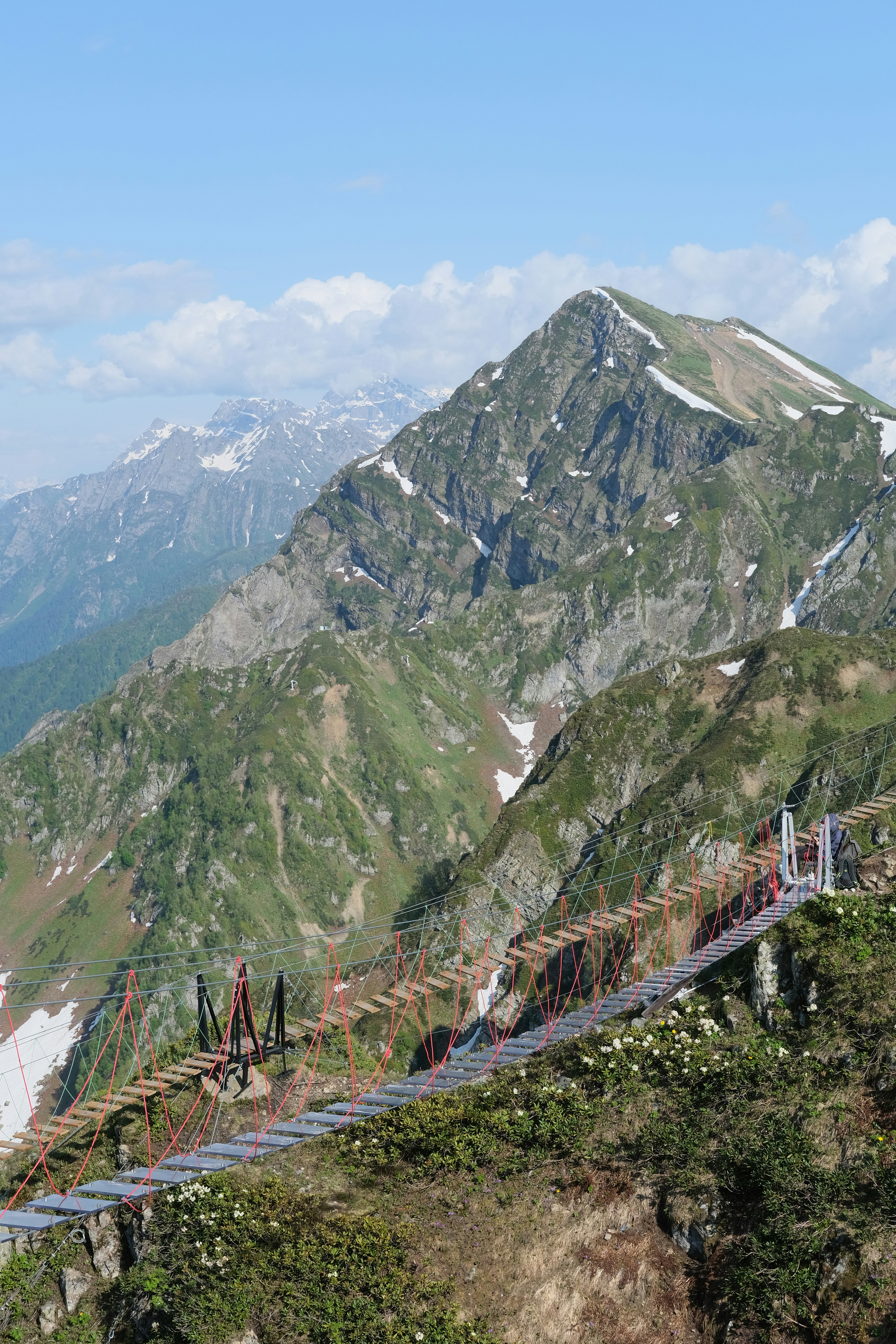 Suspension bridge crosses a green mountain slope.