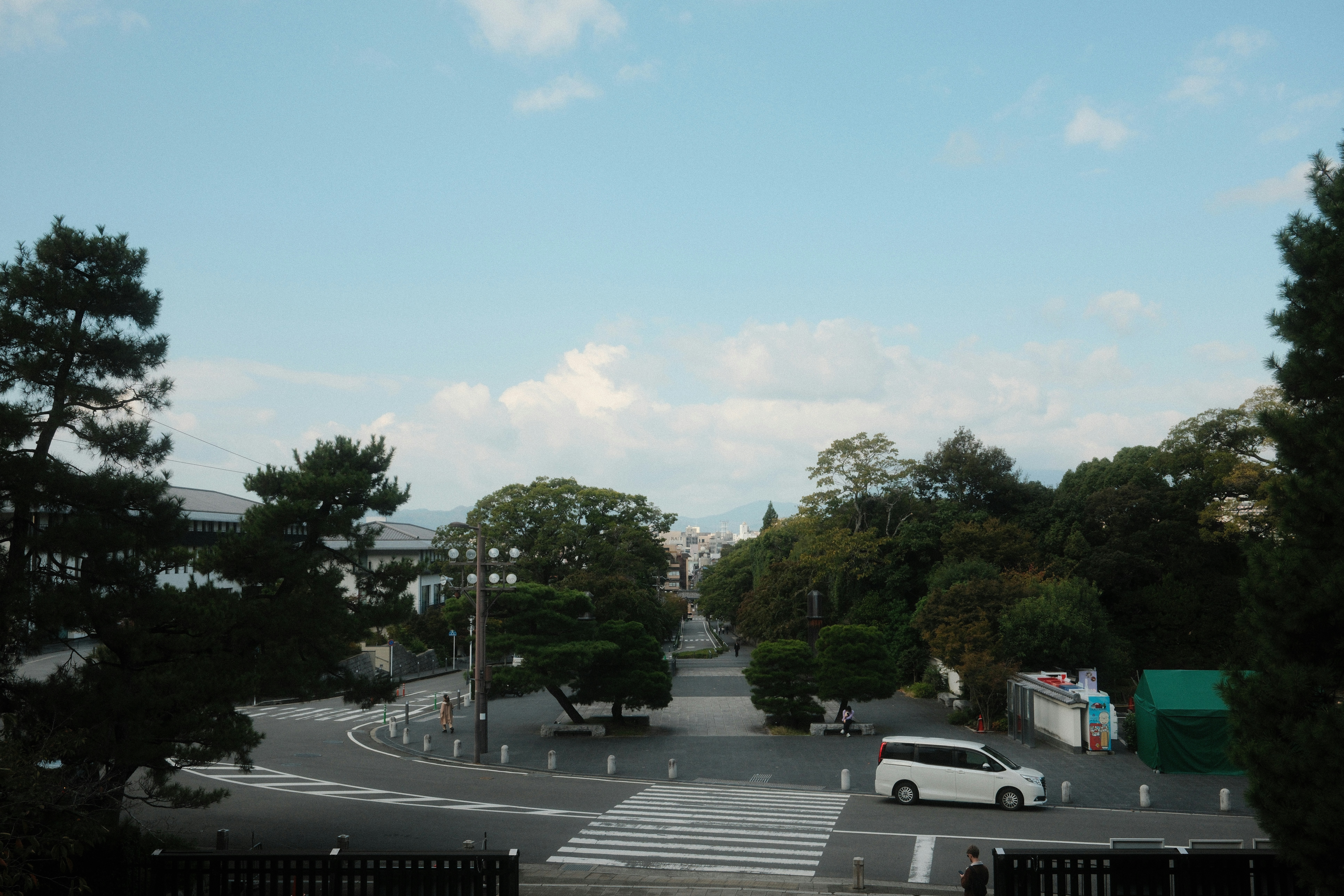 White van driving on a street with trees and sky