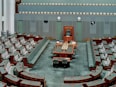 Empty parliamentary chamber with rows of seats.