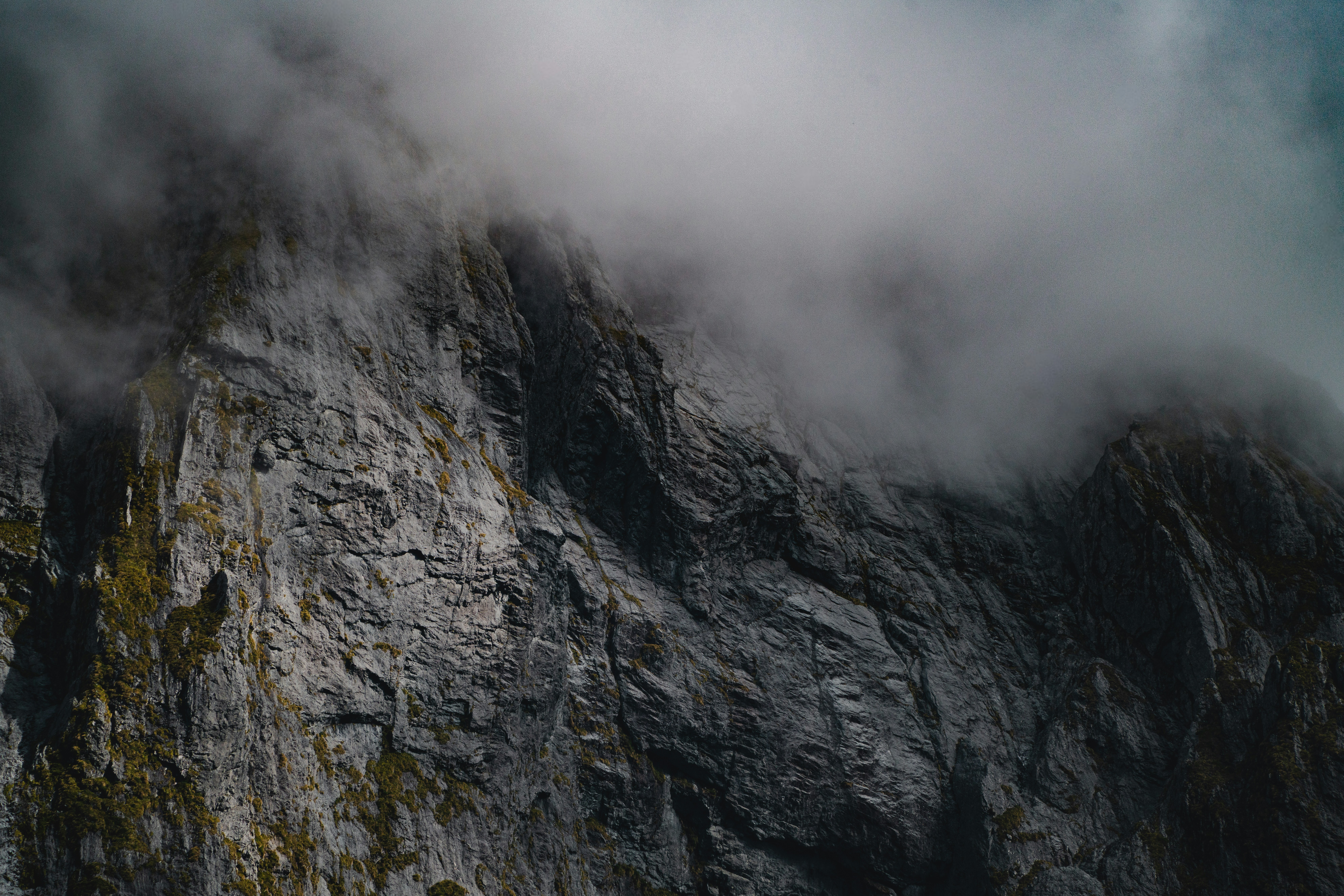 Misty clouds obscure a rugged mountain cliff face
