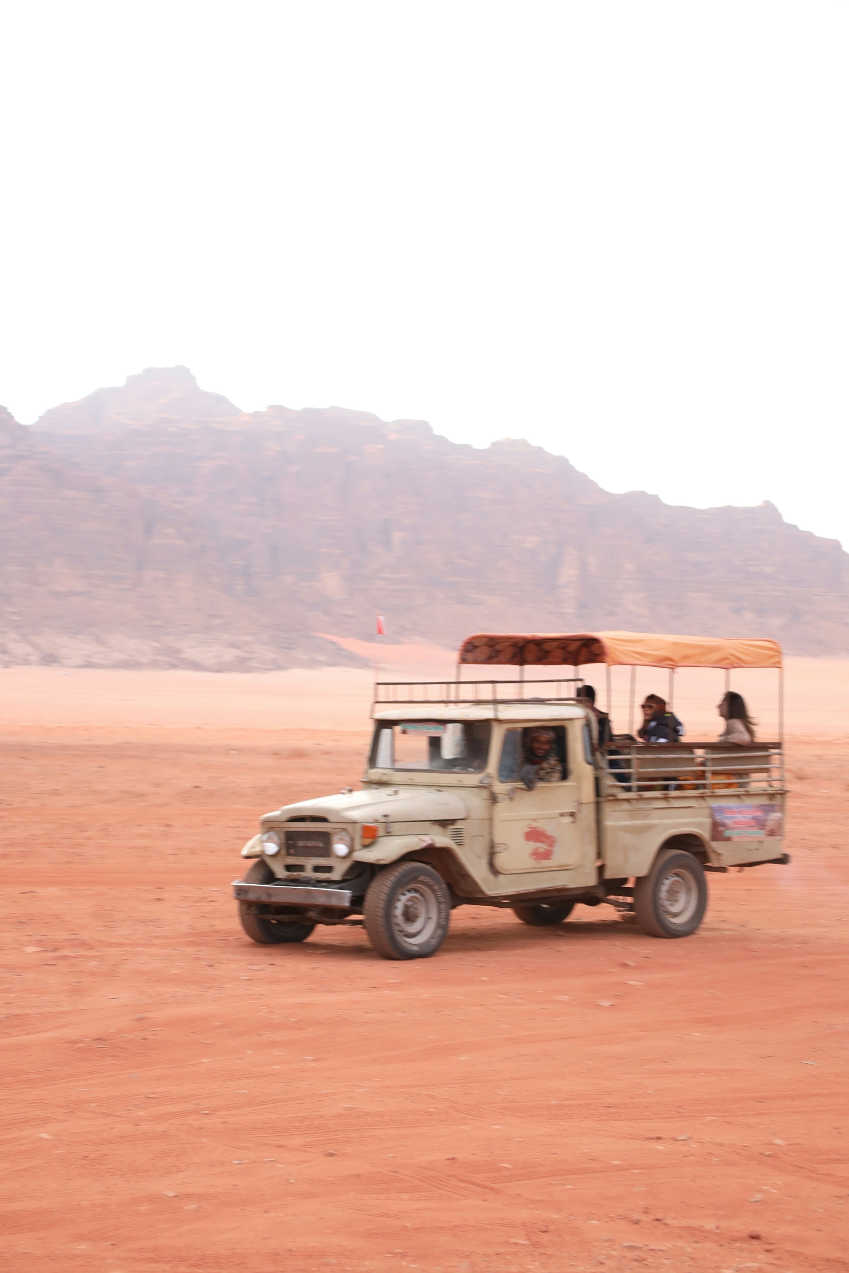 Tourists riding in an open-top jeep through desert landscape.