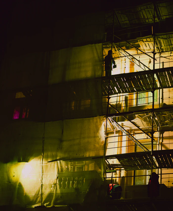 Building under construction at night with site lighting and workers
