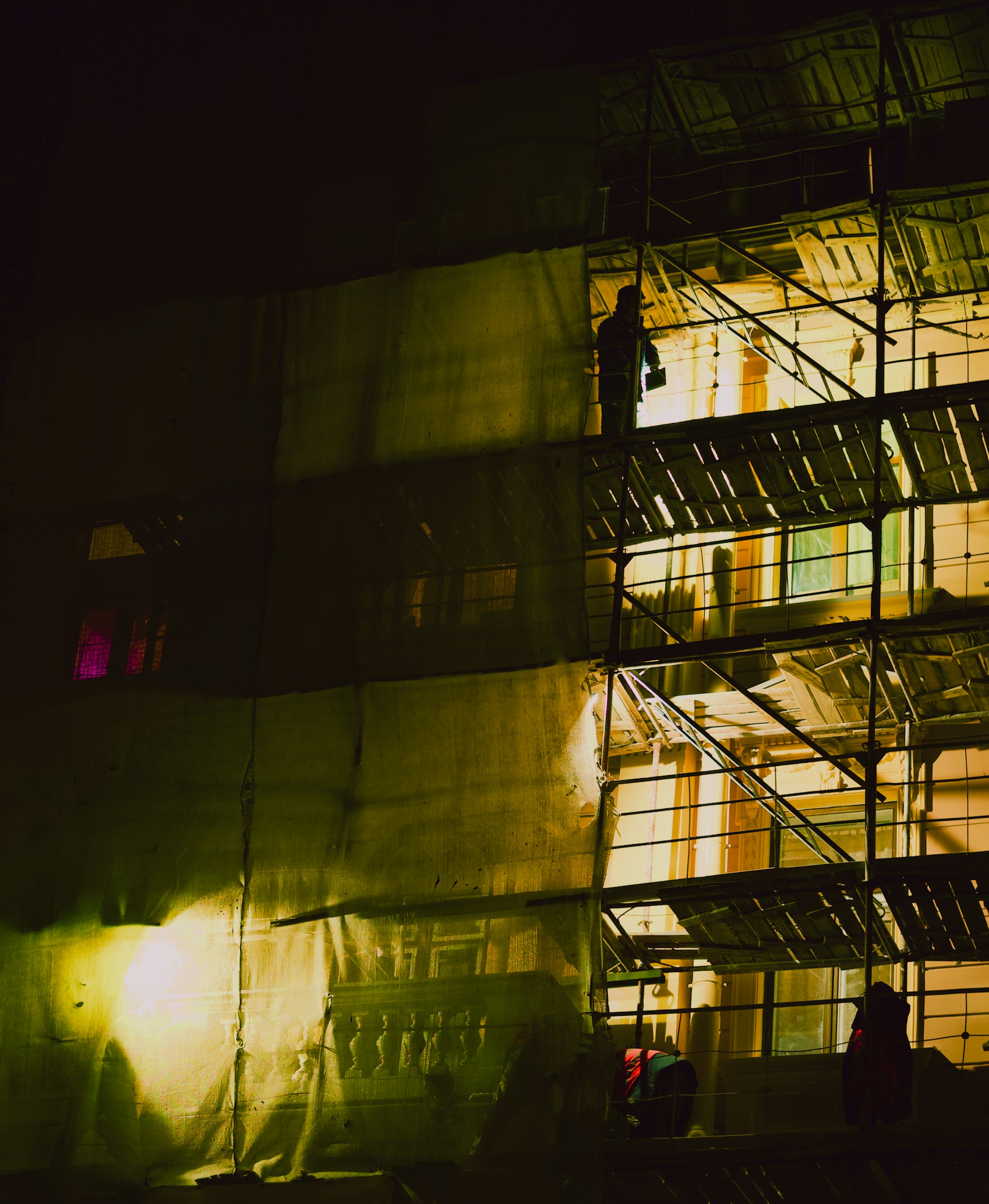 Building under construction at night with lights on-site workers.