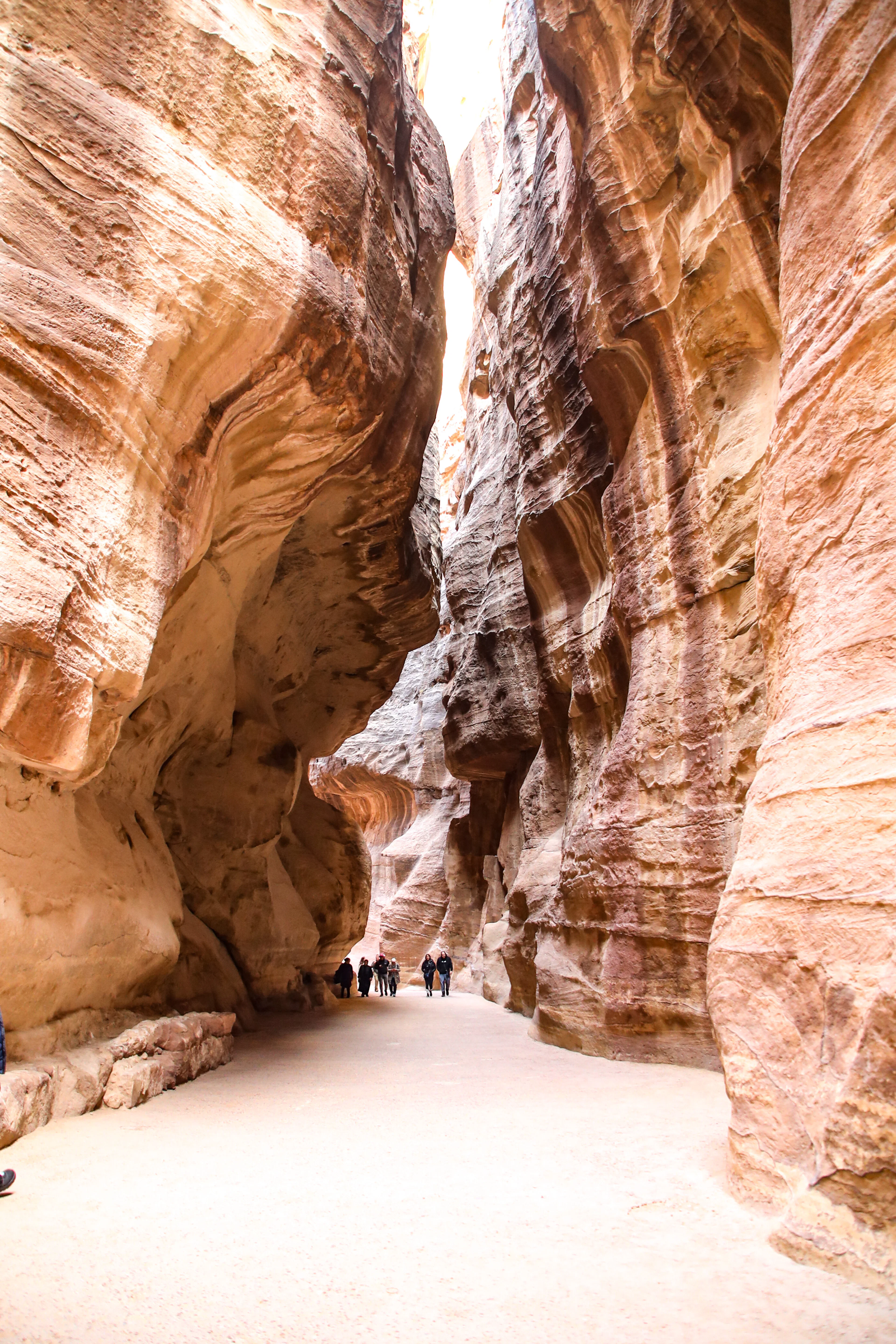 Walkers dwarfed by the towering striated sandstone walls of the Siq, the narrow gorge that leads into Petra, warm reflected light glowing off the rock