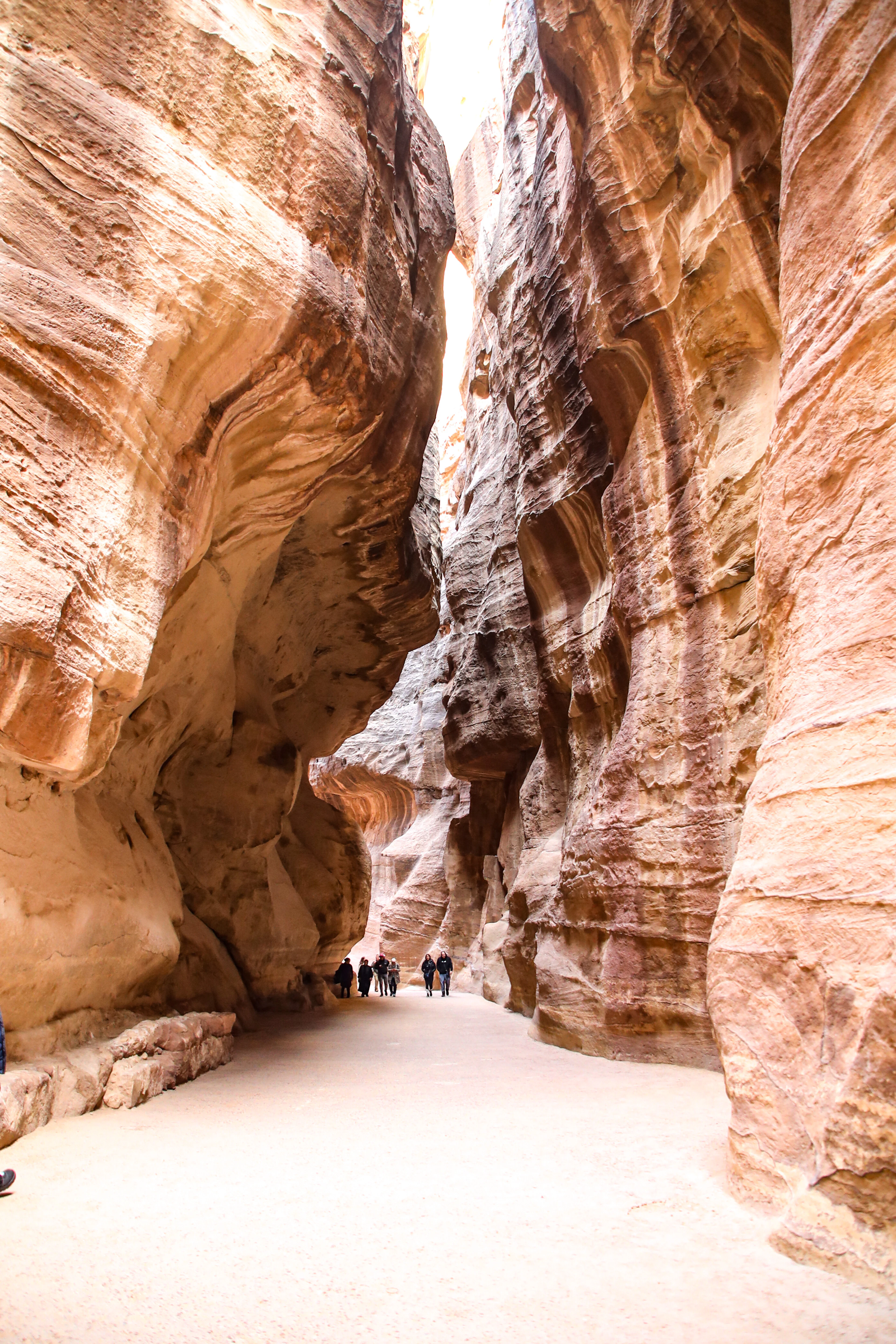 Walkers dwarfed by the towering striated sandstone walls of the Siq, the narrow gorge that leads into Petra, warm reflected light glowing off the rock