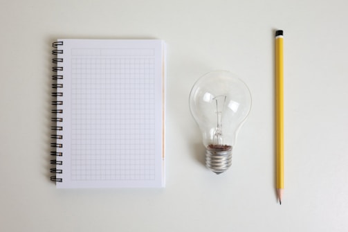 Notebook, lightbulb, and pencil on white surface.