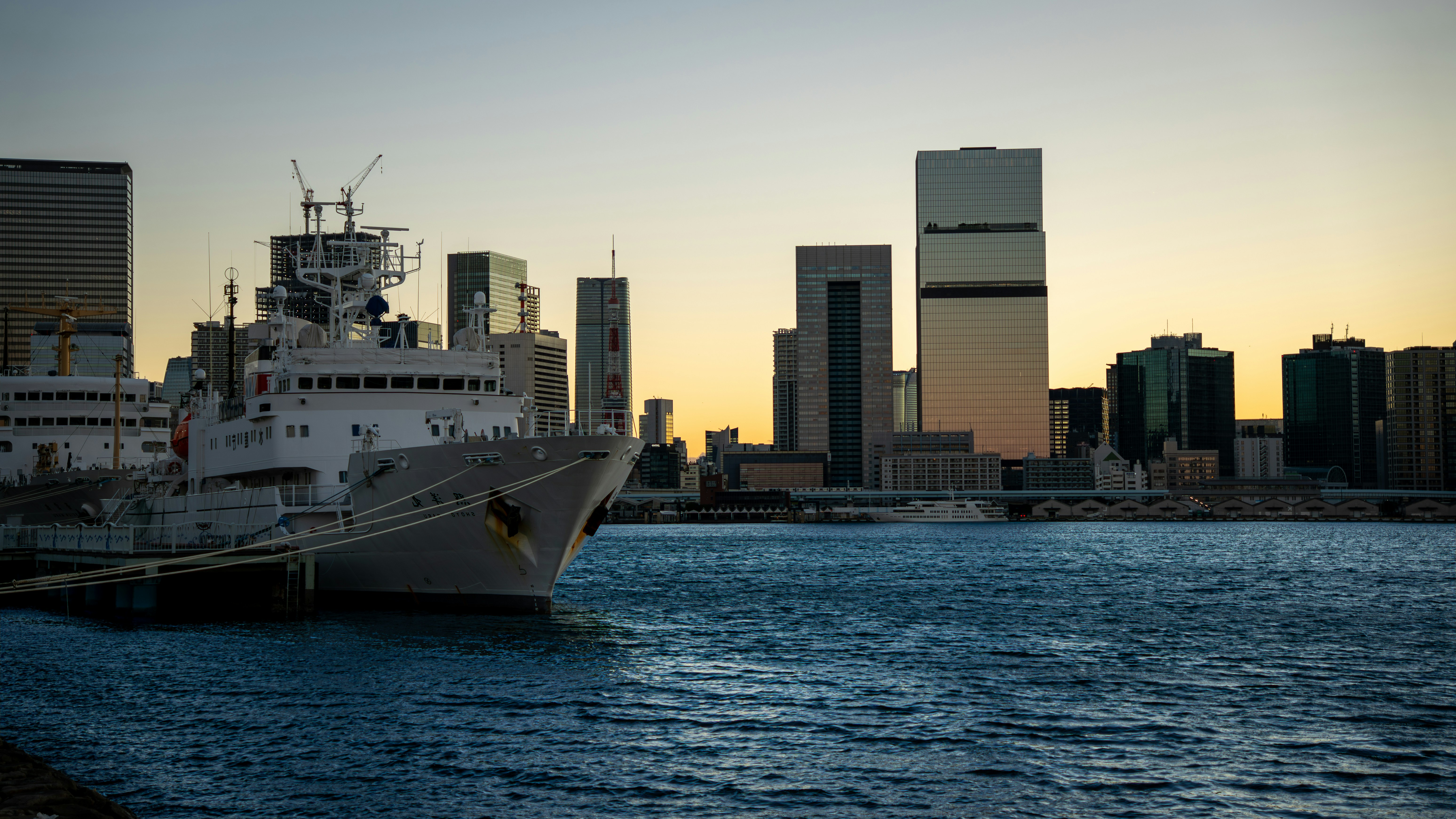 Ship docked in harbor with city skyline at sunset