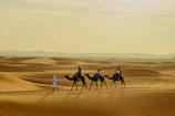 People riding camels through desert sand dunes
