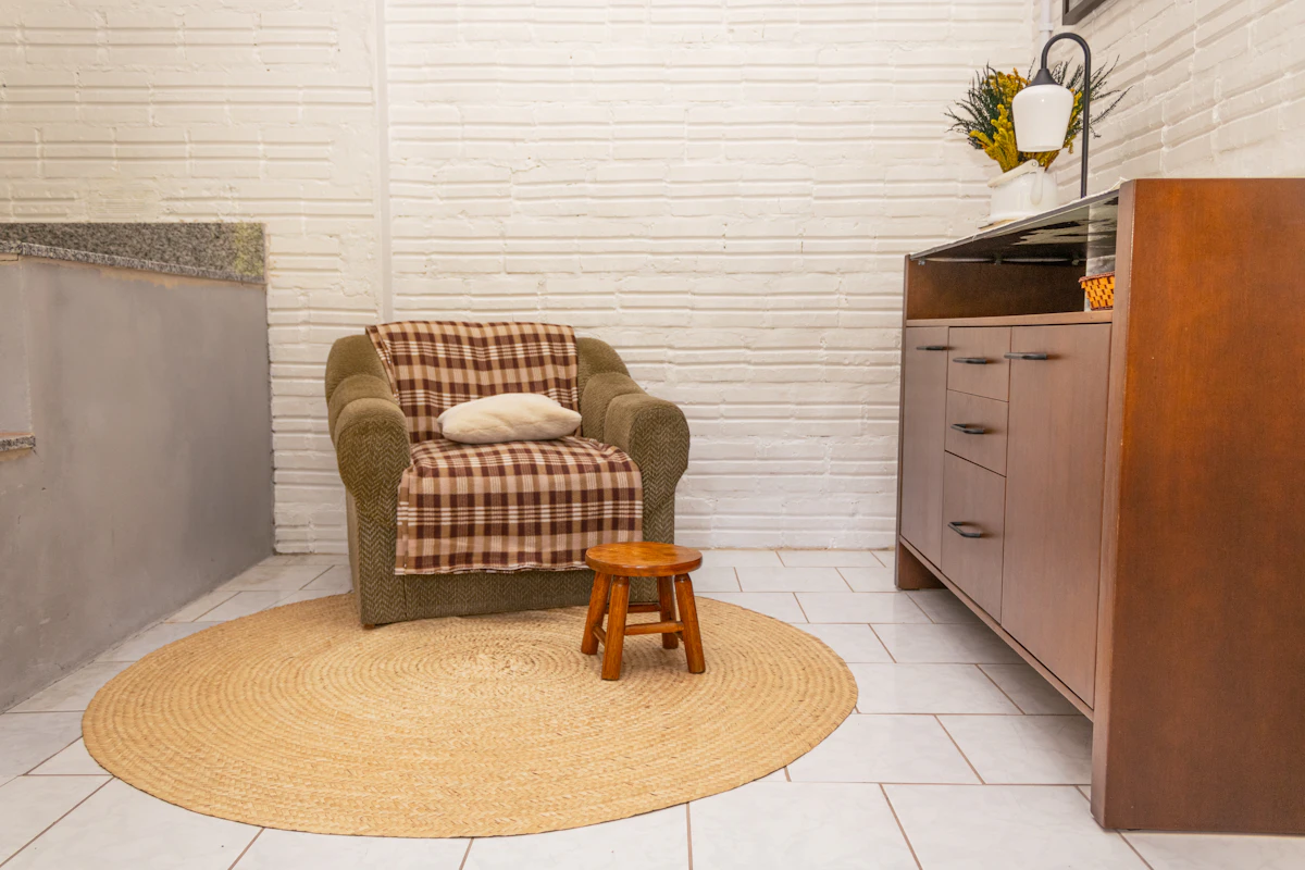 Cosy armchair with a folded blanket and a small wooden stool resting on a textured rug