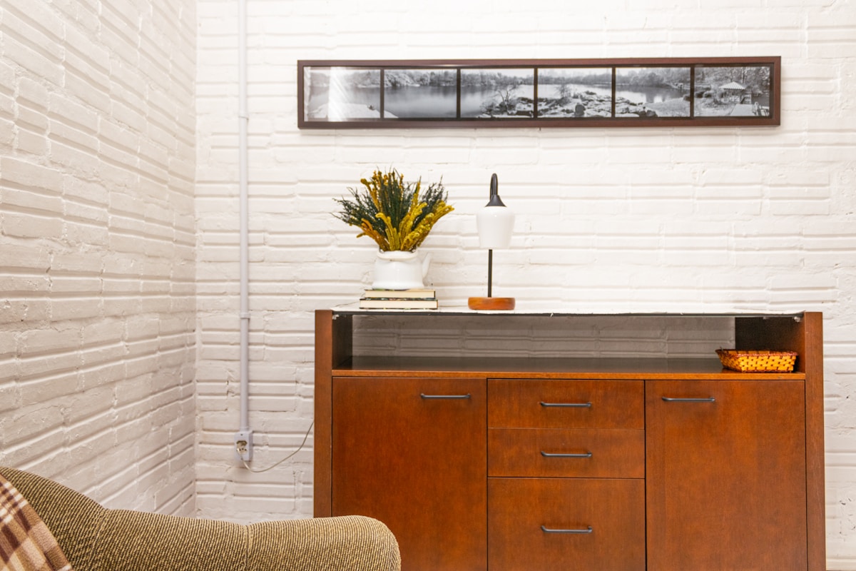 vintage wooden dresser styled with lamp and yellow flowers against white brick wall