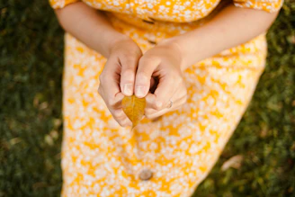Woman in yellow dress holds a fallen leaf