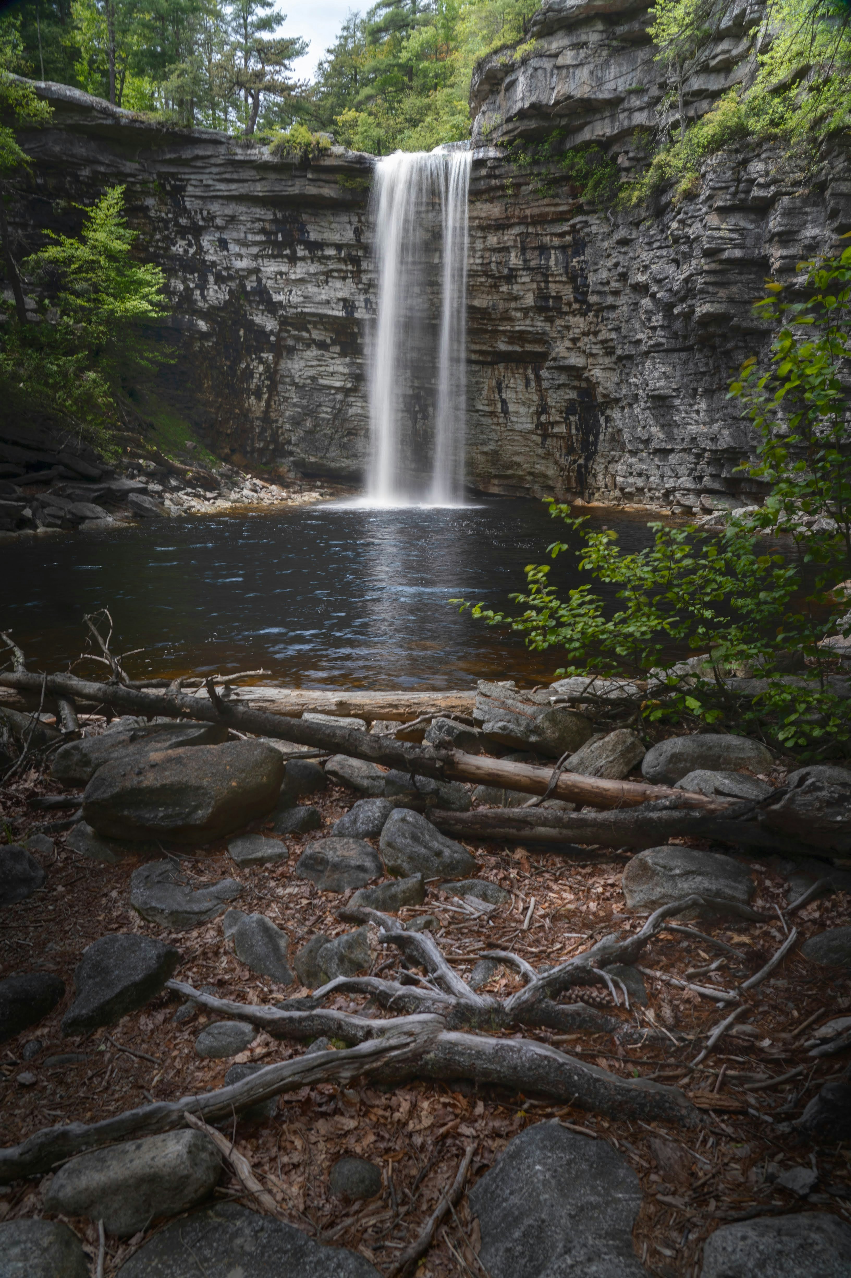 Tall waterfall cascades into a dark pool surrounded by rocks.