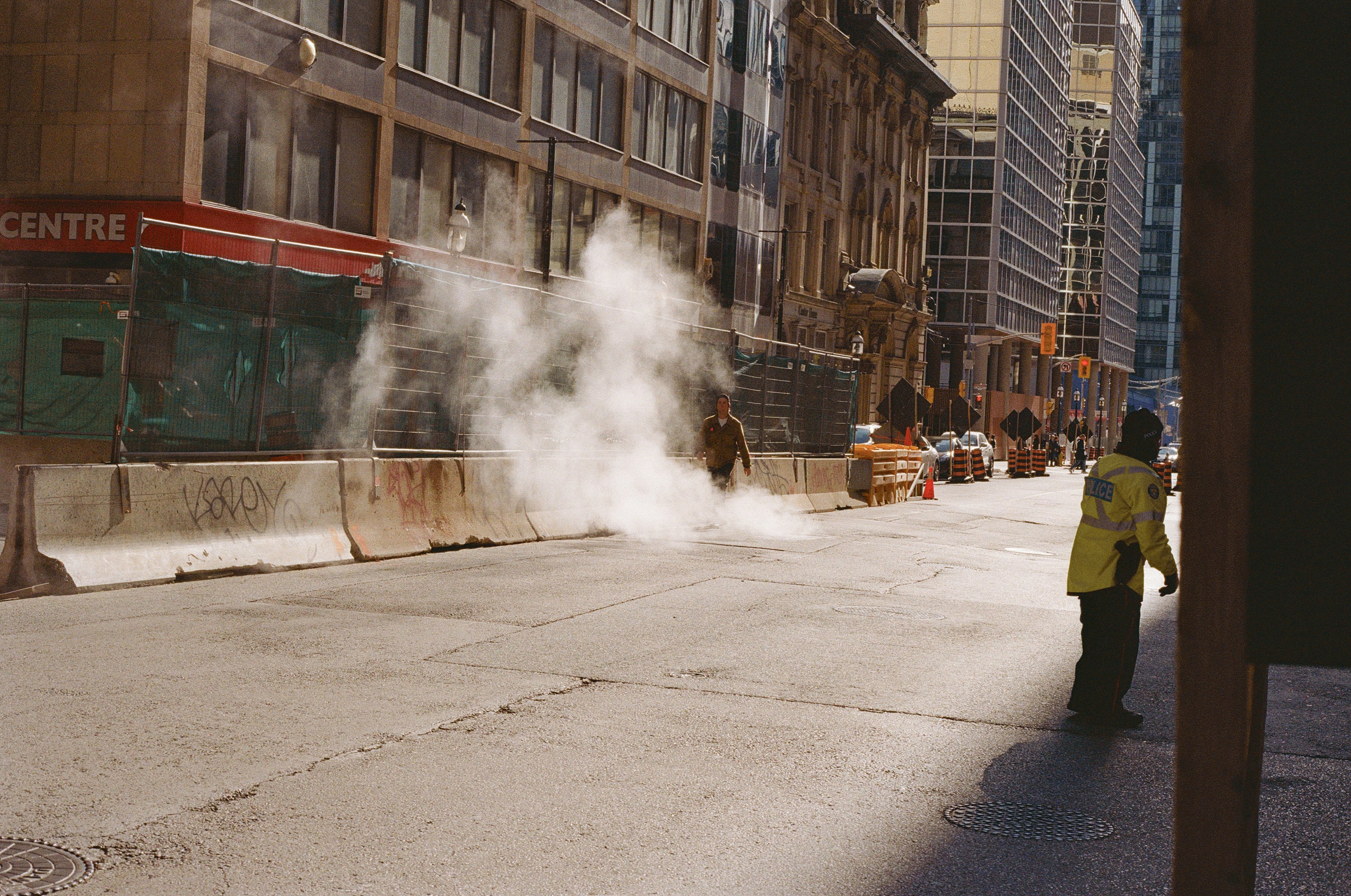 Steam erupts from a city street with construction barriers.