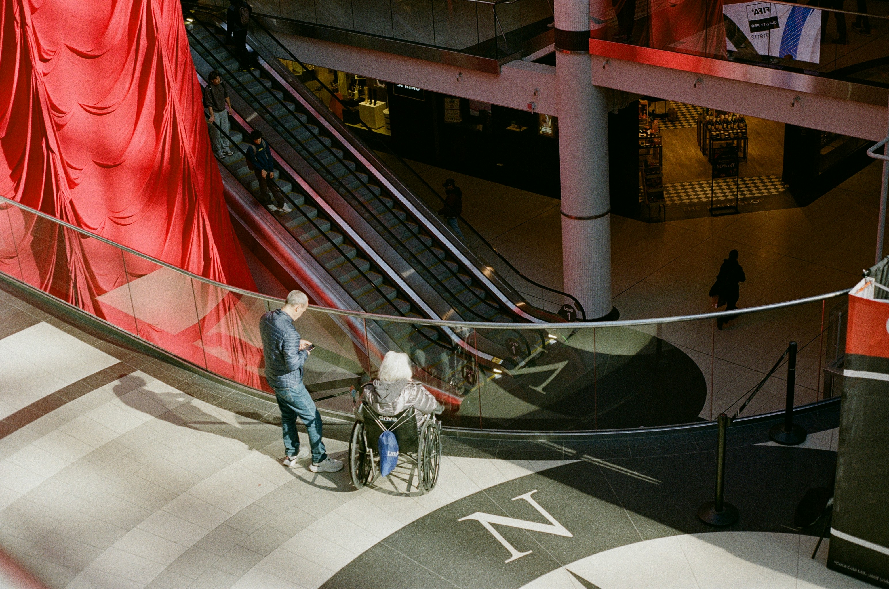 People on escalator and wheelchair in shopping mall.