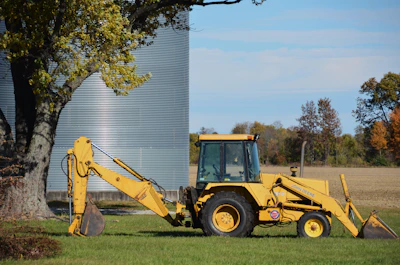 Yellow backhoe parked next to a large silo