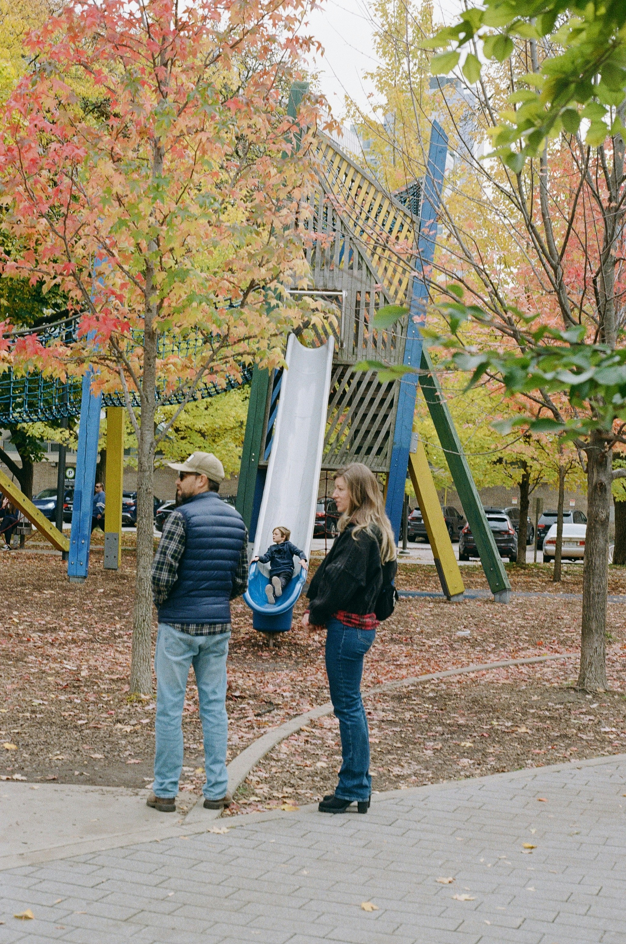 Adults watch child on playground slide during autumn