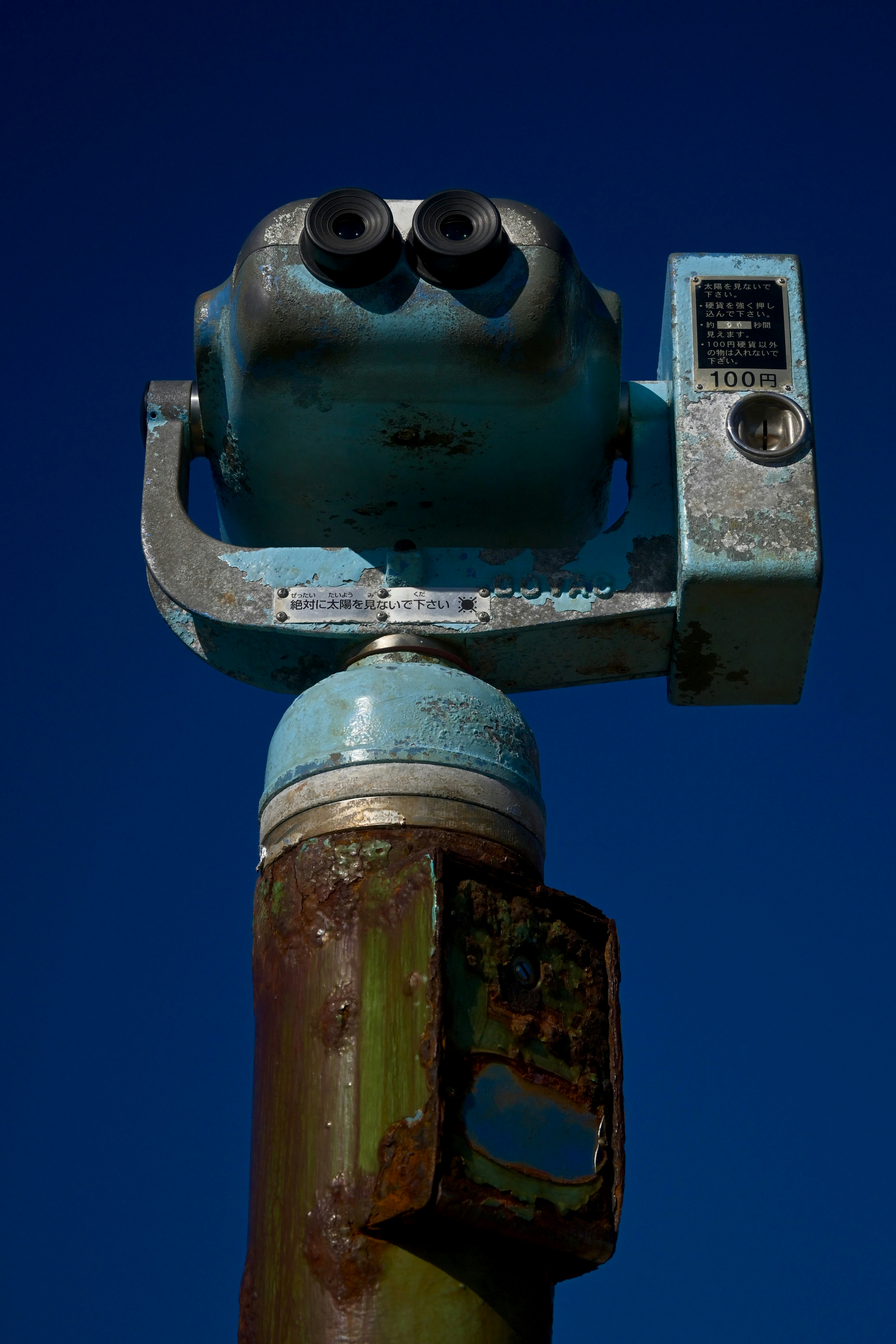 A weathered blue coin-operated viewer against a clear blue sky