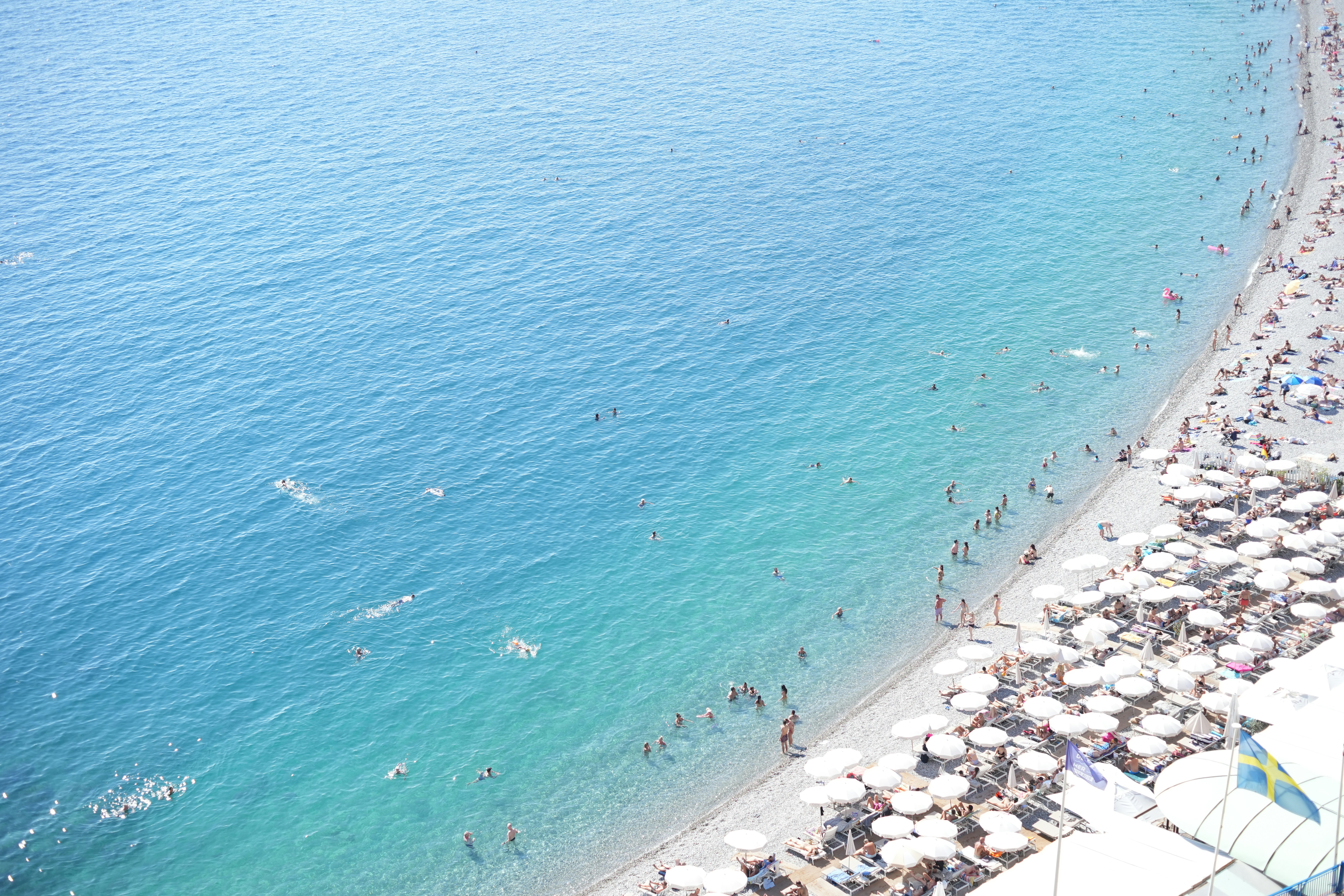 Crowded beach with people swimming in clear blue water.