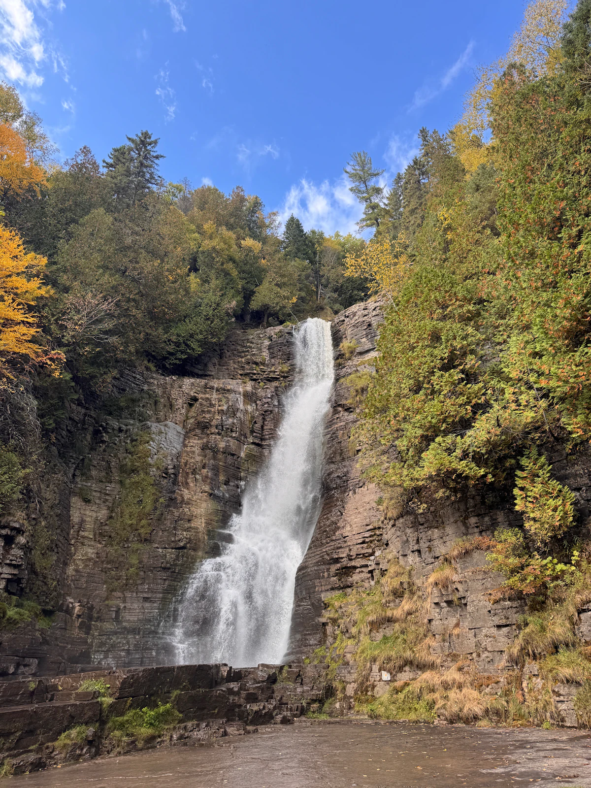 A waterfall over layered rock among autumn trees near La Malbaie