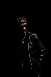 Man in leather jacket and baseball cap.