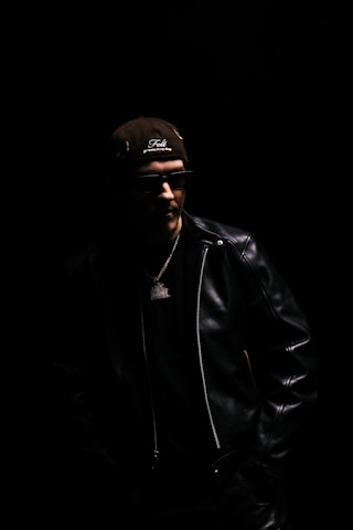 Man in leather jacket and baseball cap.