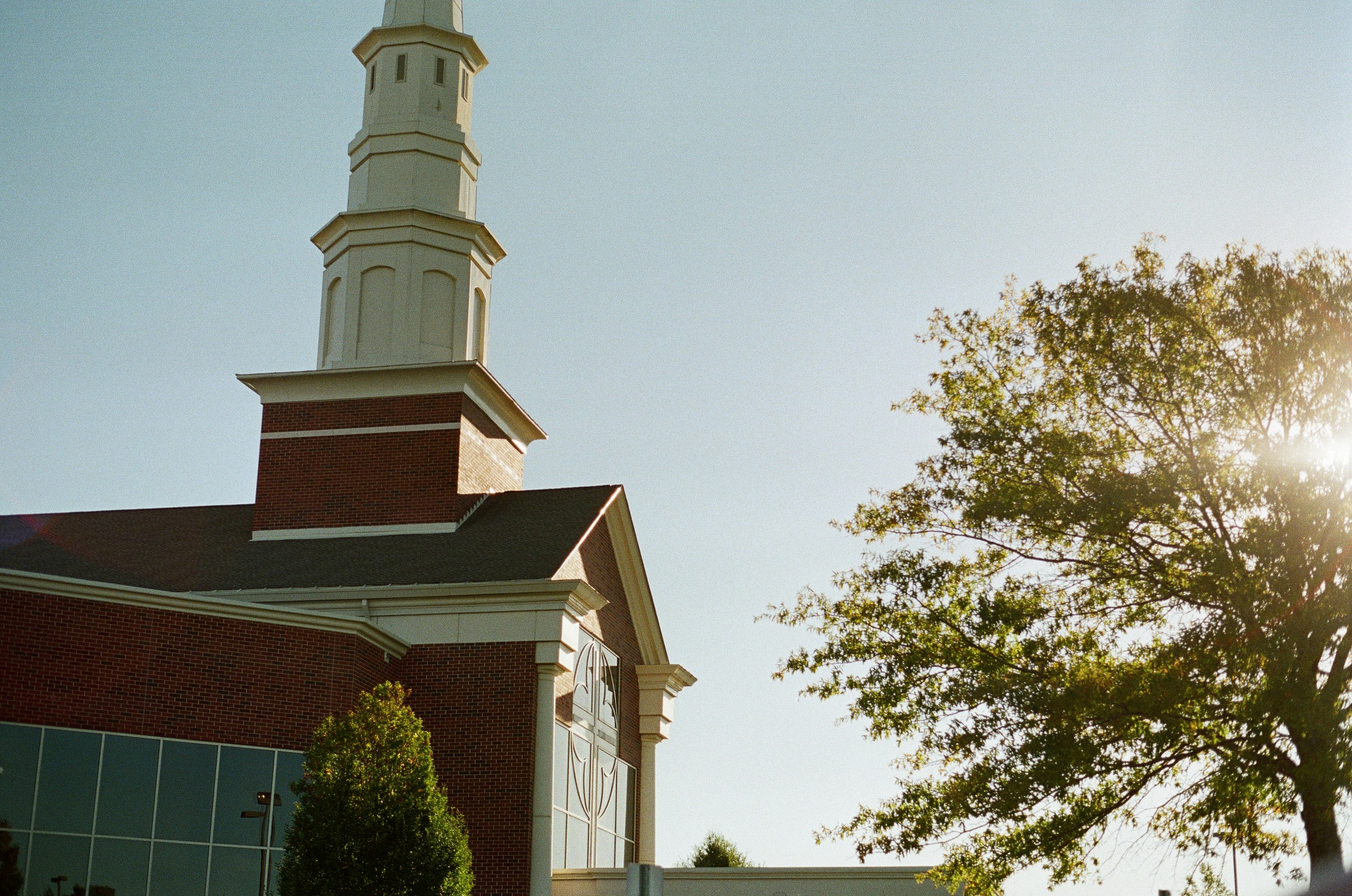 Brick building with a tall white steeple and trees.
