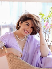 A smiling woman in a lavender sari with jewelry.