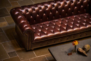 A brown leather chesterfield sofa with a small vase