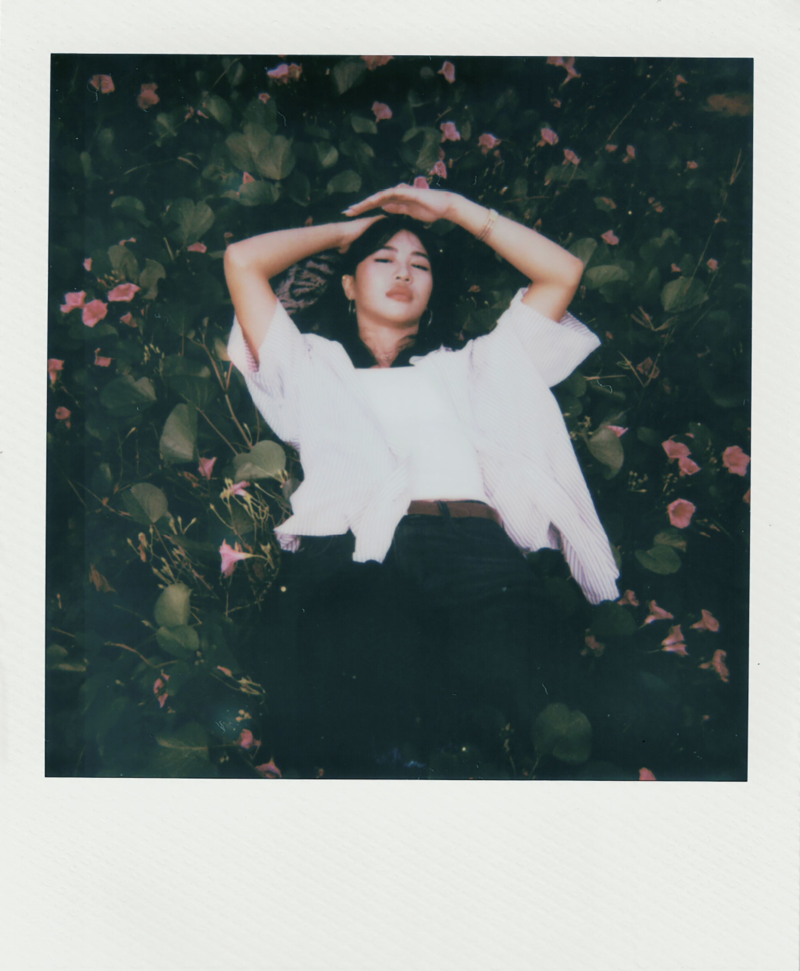 Young woman lying in green foliage with pink flowers.