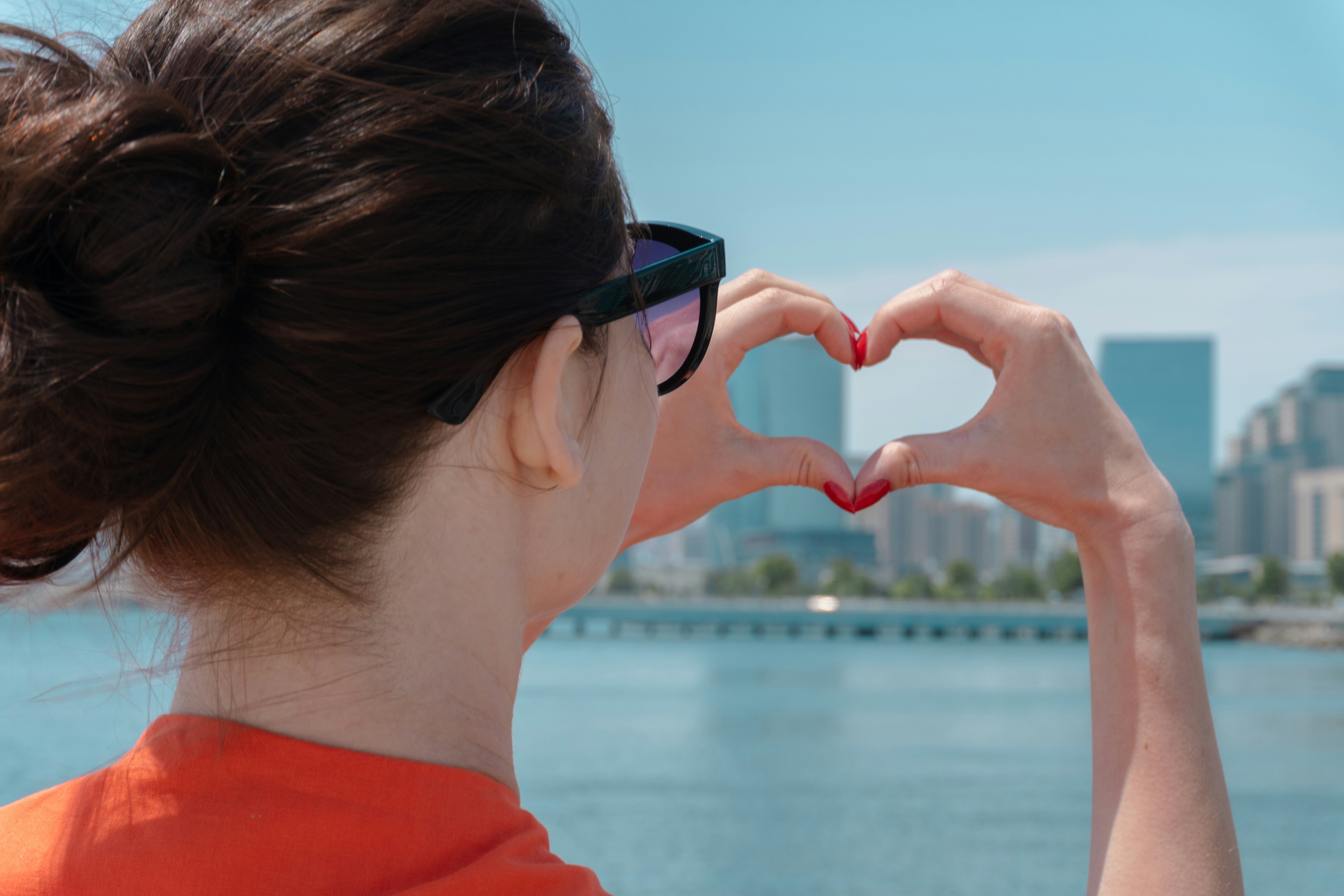 Woman makes heart shape with hands over cityscape