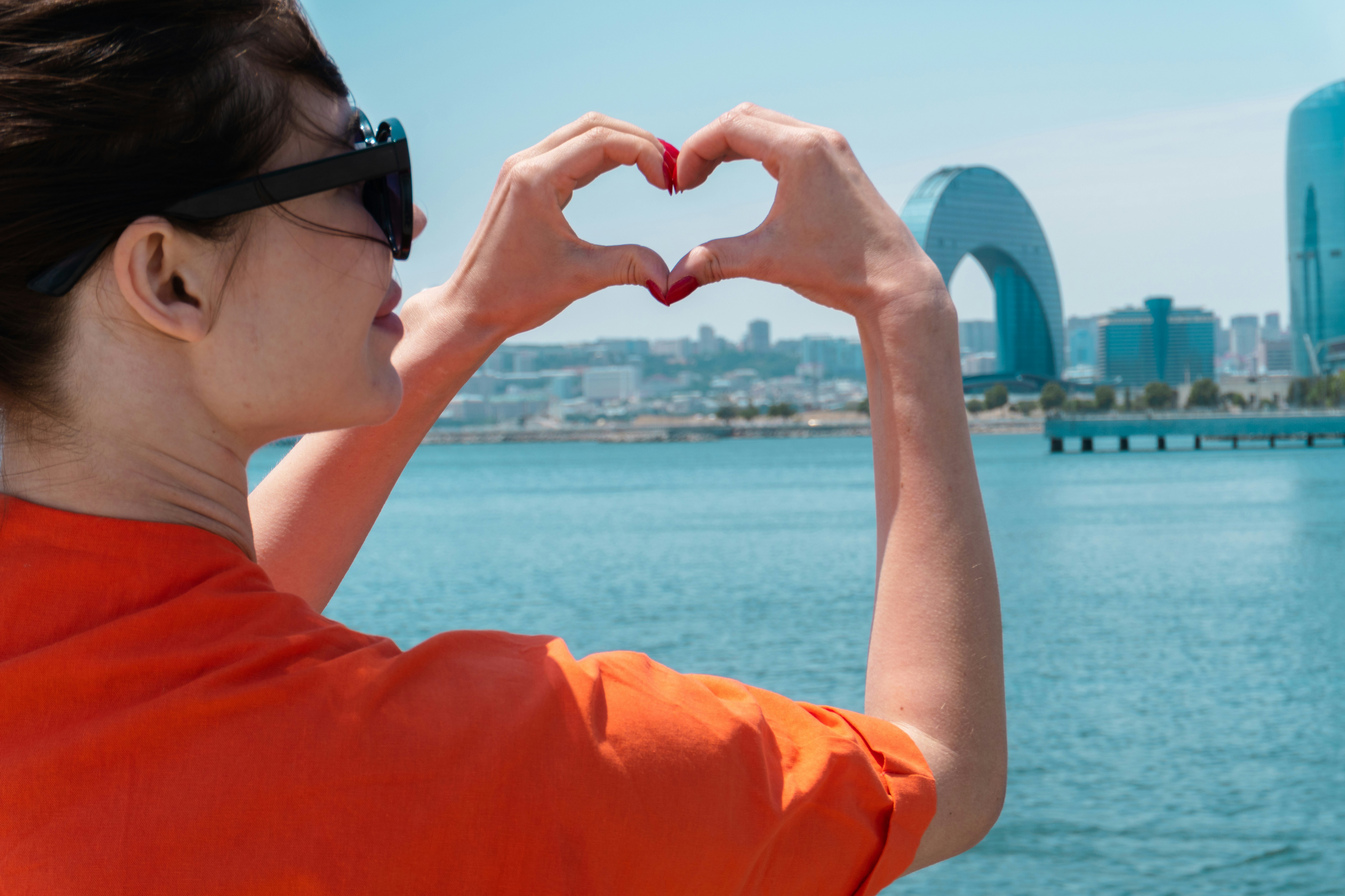 Woman makes heart shape with hands overlooking city.