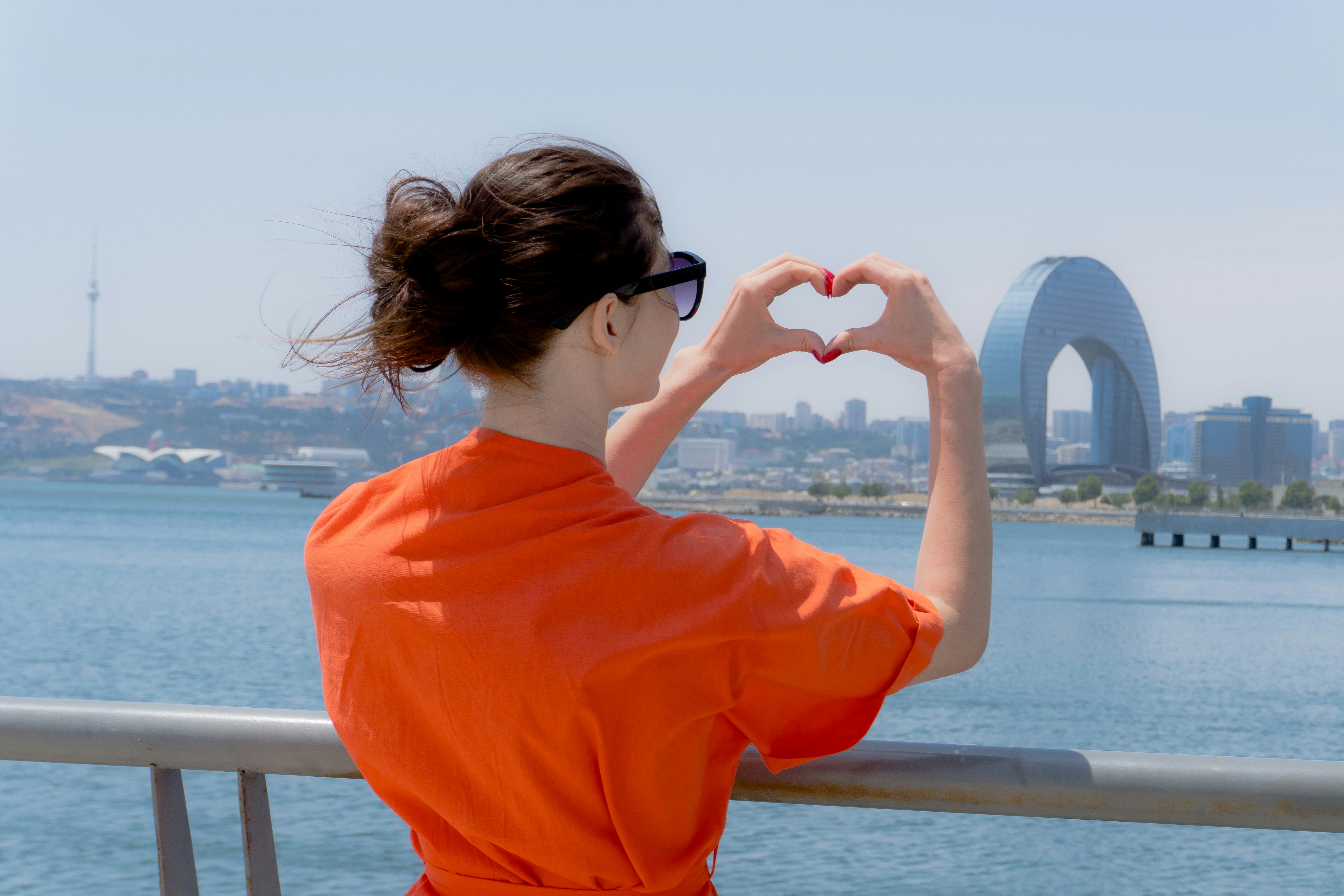 Woman makes heart shape with hands overlooking city skyline