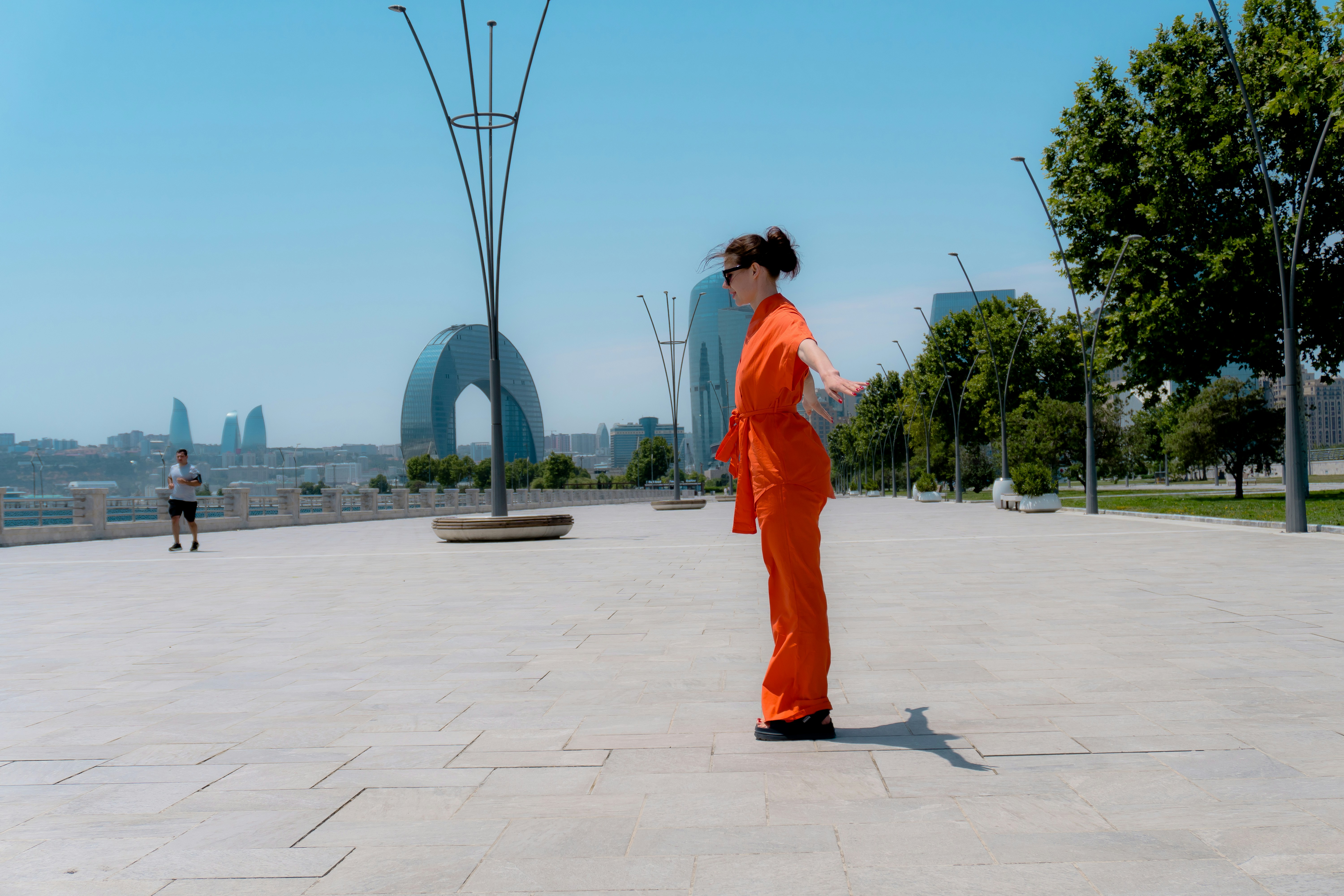 Frau im orangefarbenen Overall steht auf einem gepflasterten Platz.