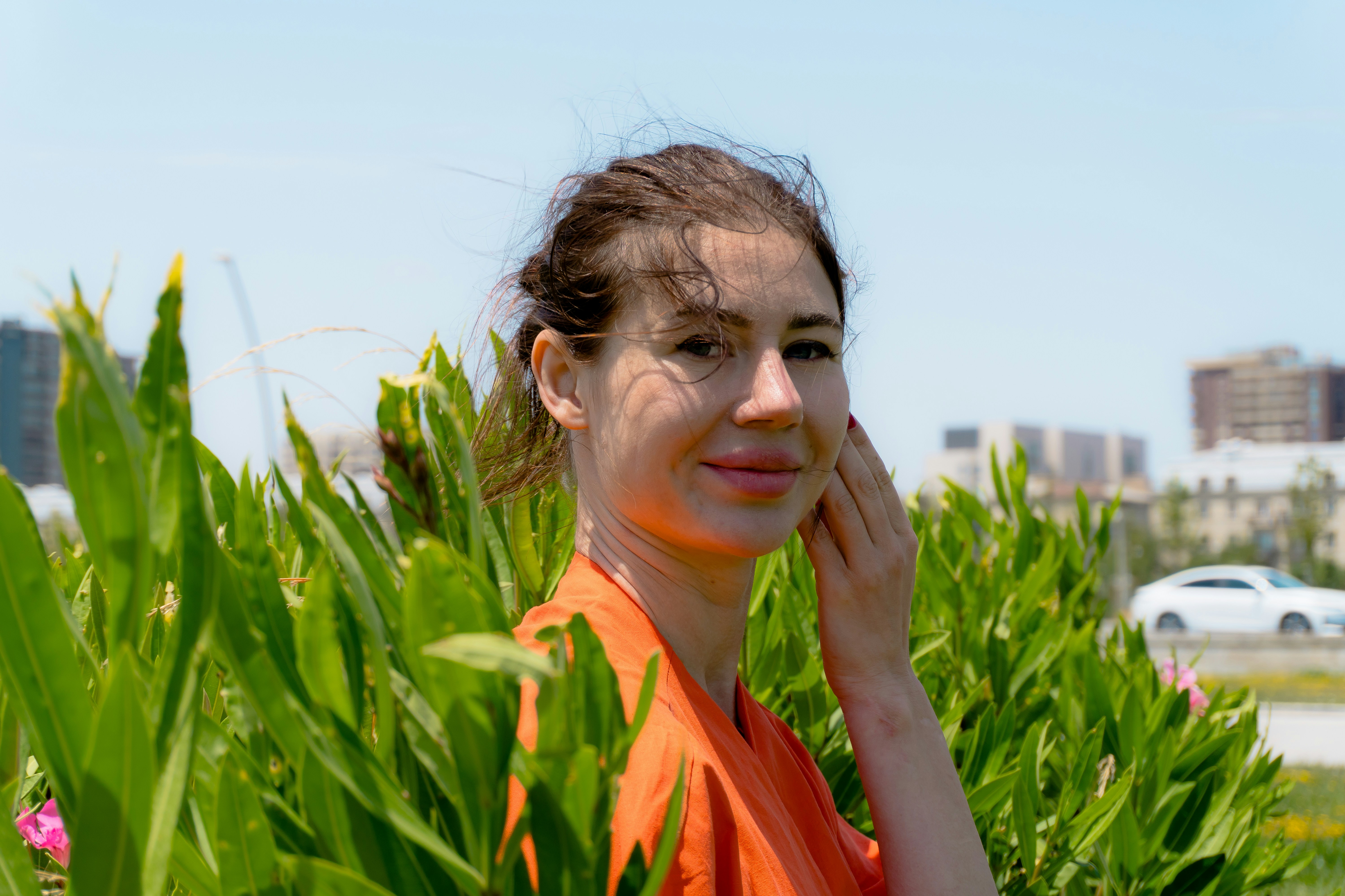 Young woman in orange shirt behind green plants