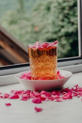 Glass of amber liquid with pink rose petals