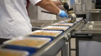 Worker filling food trays on a conveyor belt.