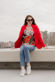 Woman in red blazer and jeans sitting outdoors.