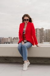 Woman in red blazer and jeans sitting outdoors