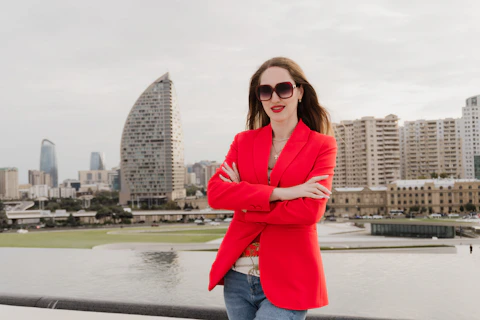 Woman in red blazer with arms crossed, city skyline.