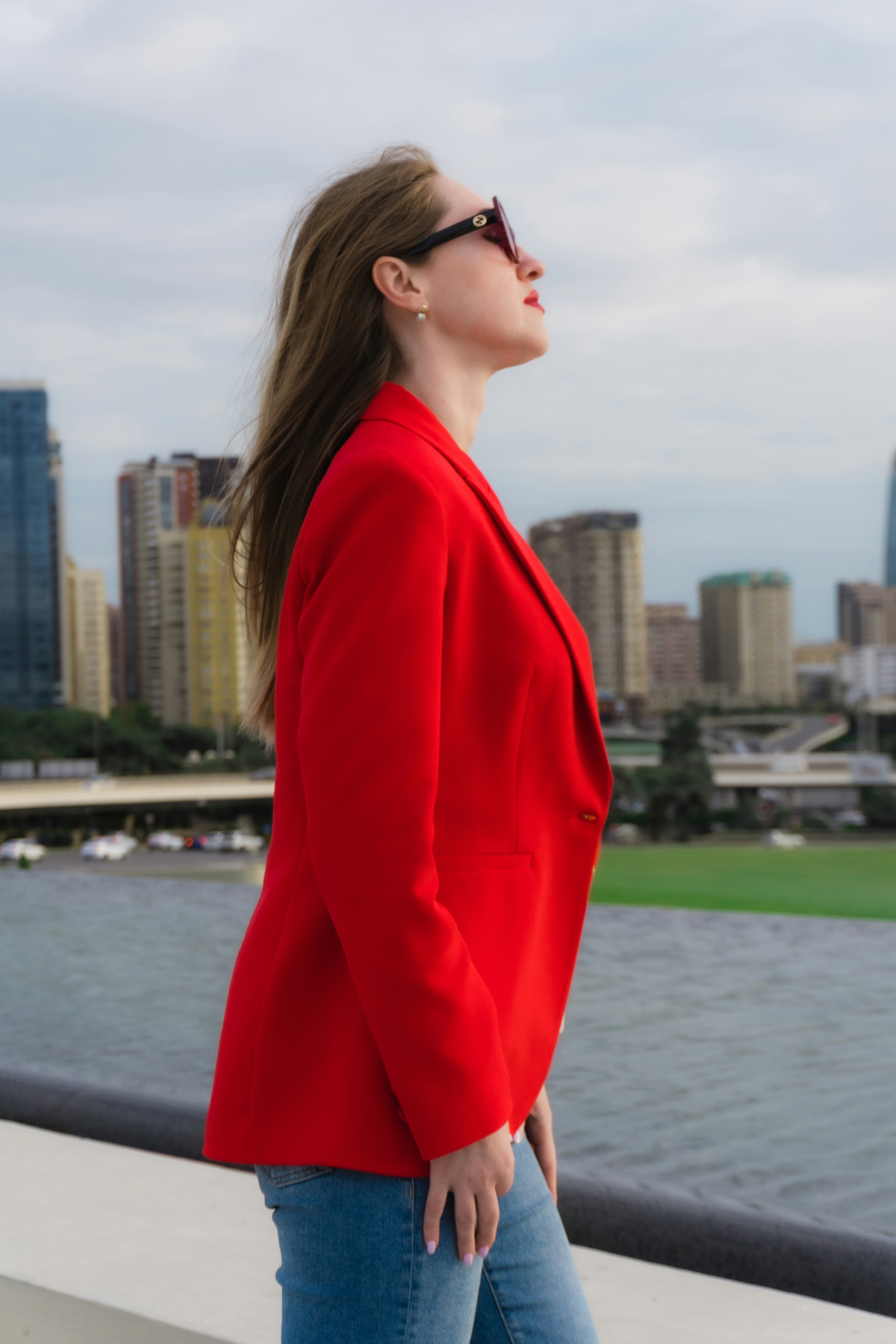 Woman in red blazer looking up at city skyline