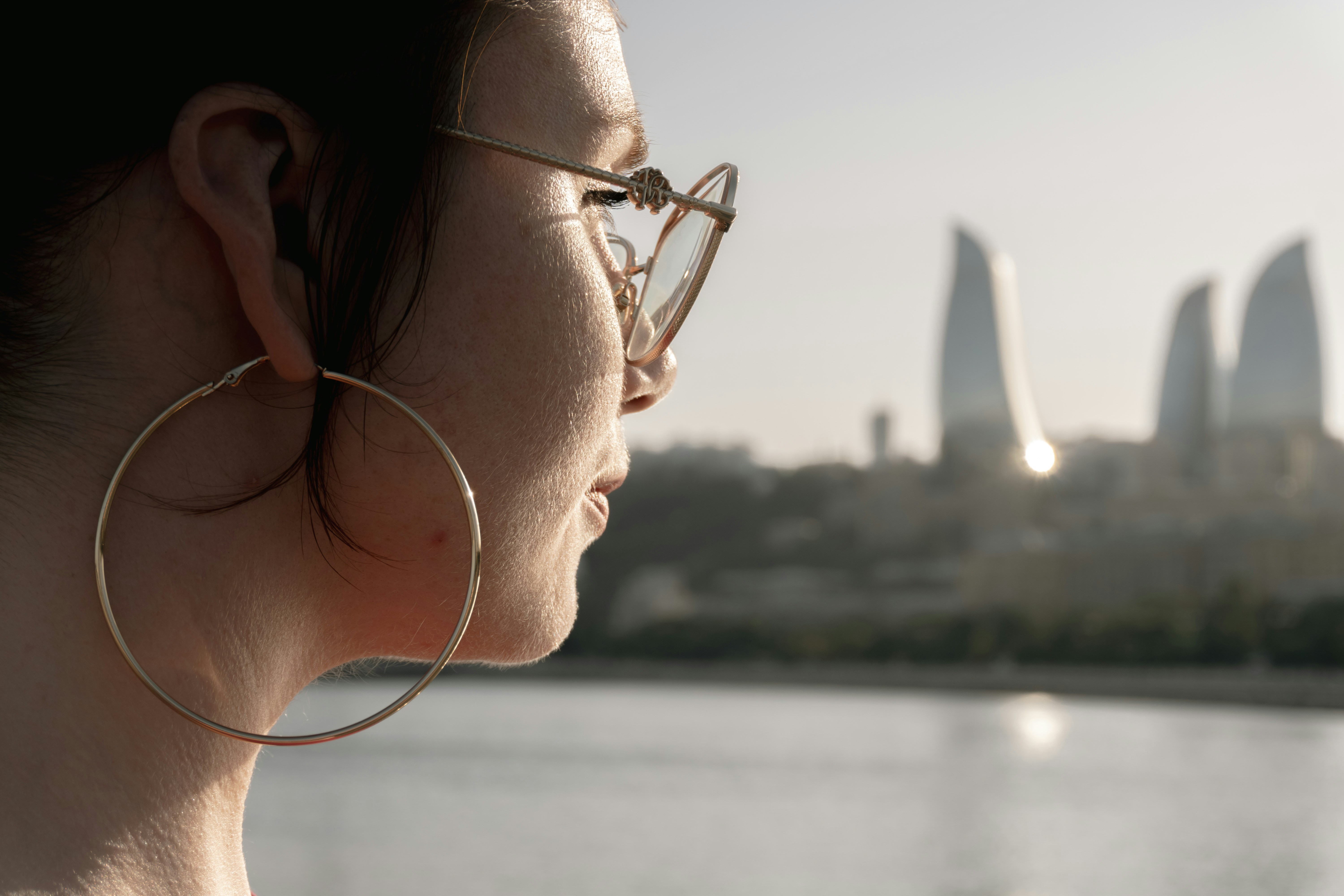Woman with large hoop earrings and sunglasses overlooking city skyline