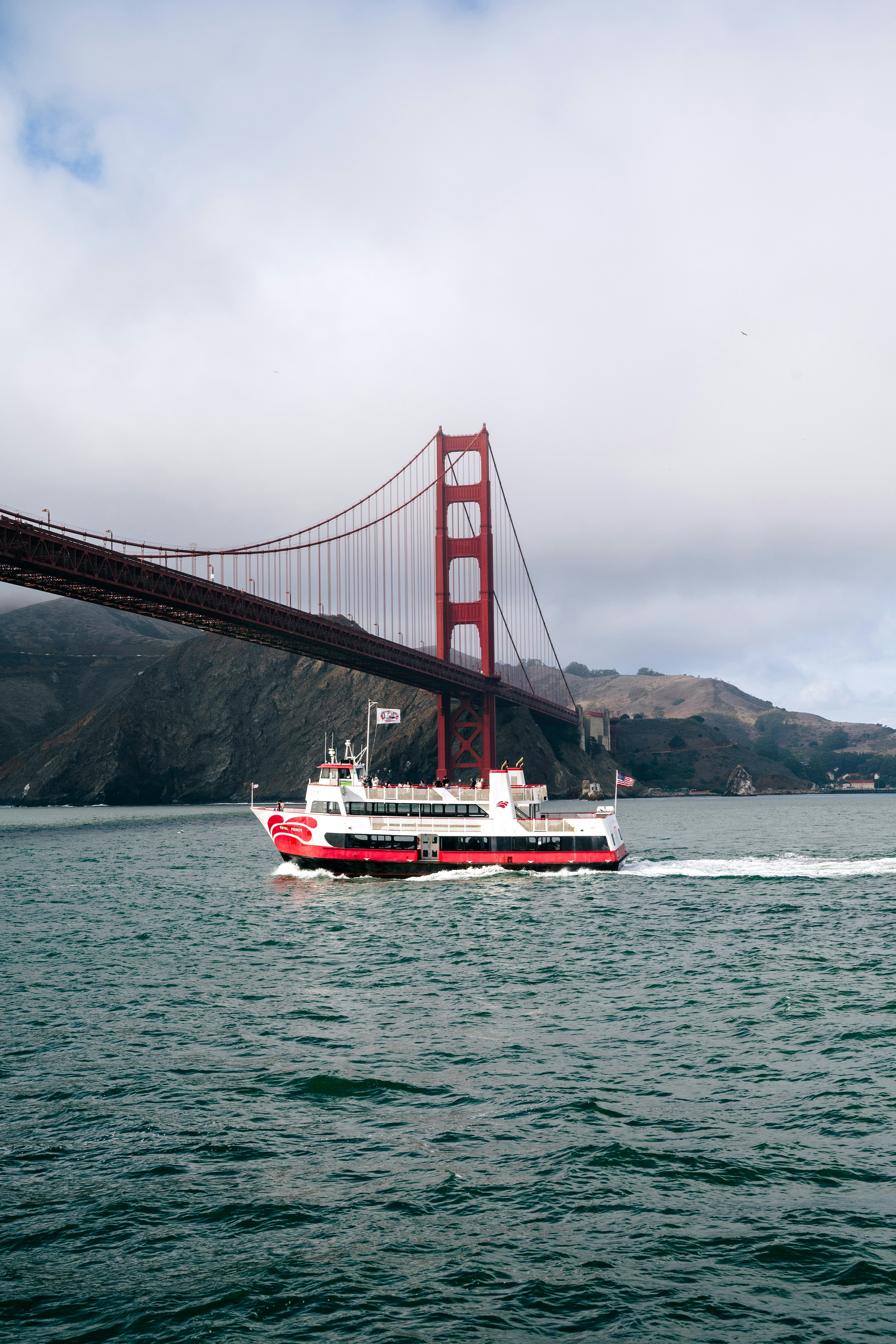 Red and white ferry boat sails under golden gate bridge