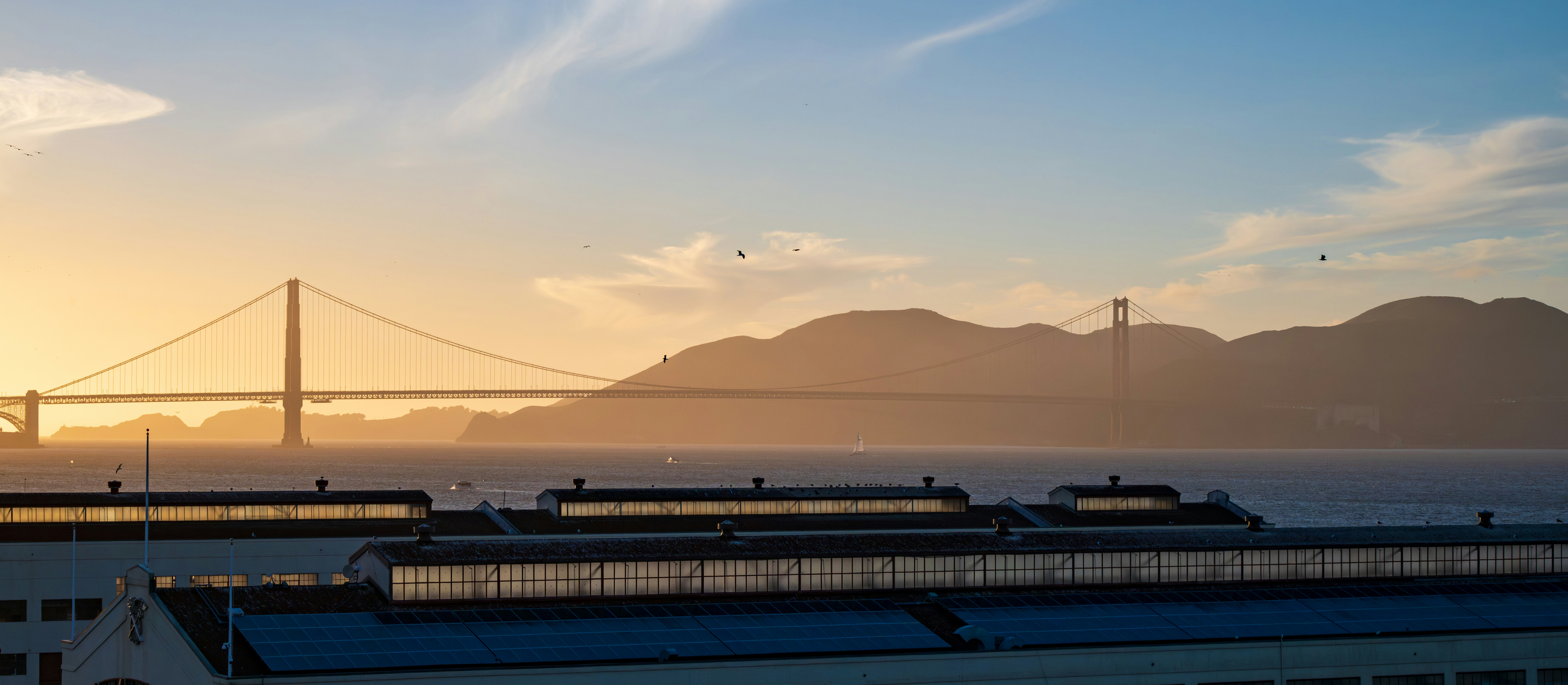 Golden gate bridge at sunset with distant hills.