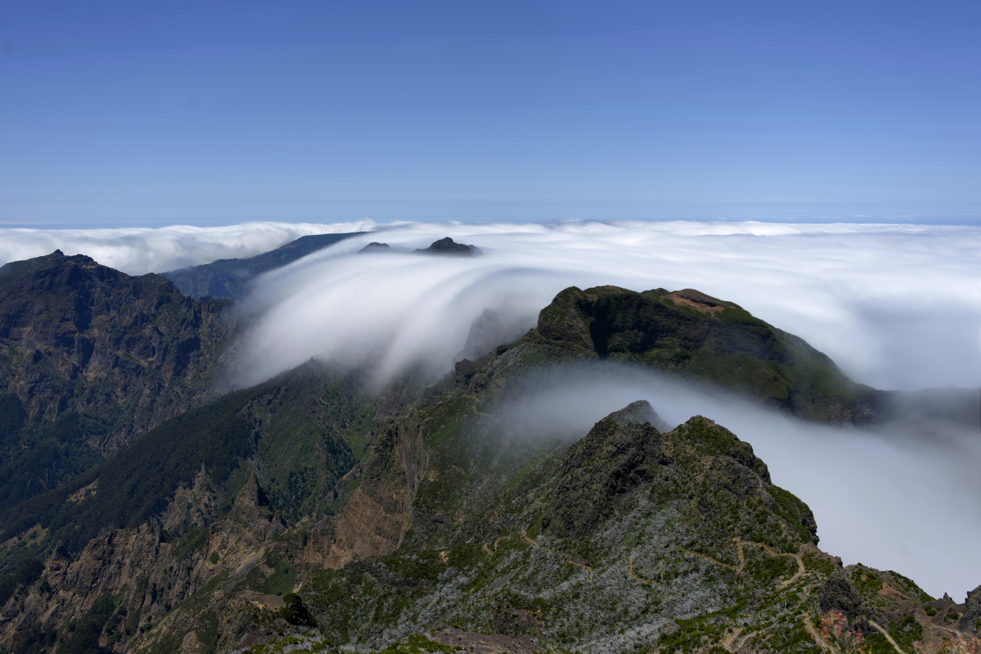 Clouds flowing over rugged mountain peaks under a clear sky