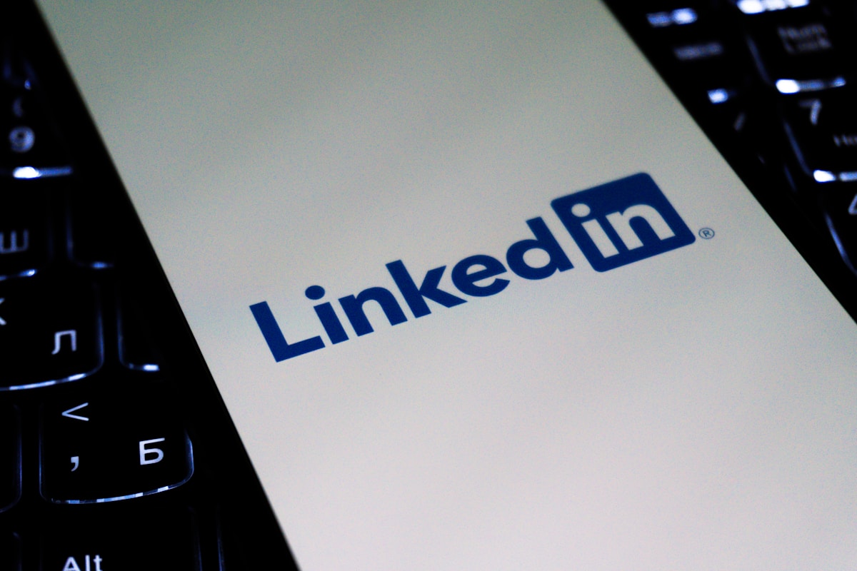 Logotipo do LinkedIn em um celular posicionado sobre o teclado de um laptop.