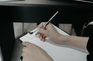 Person writing on a clipboard with a pen.