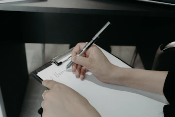 Person writing on a clipboard with a pen.