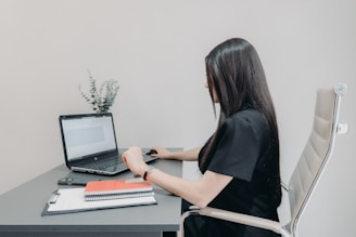 Woman working on laptop at desk with notebooks.
