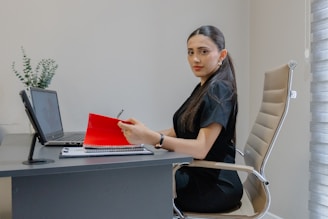 Woman working at desk with laptop and red folder.